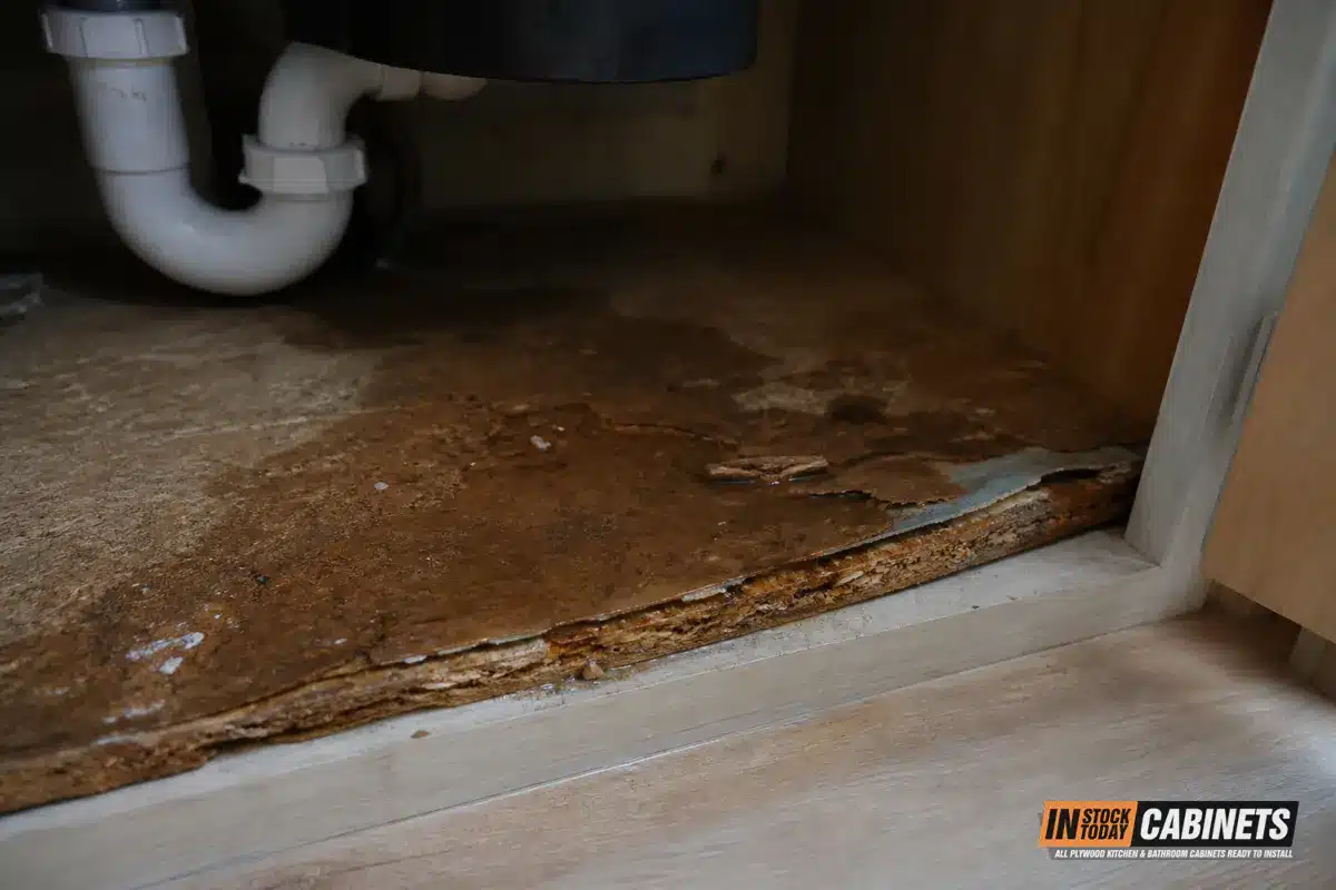 Swollen and delaminating particle board on the bottom panel of a kitchen sink base cabinet after a slow water leak
