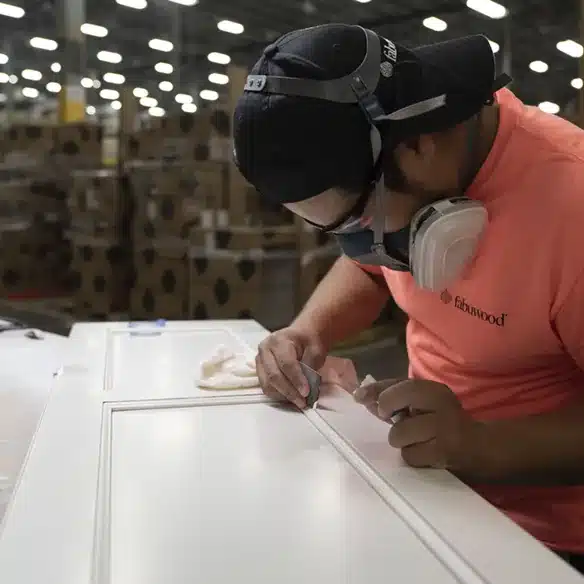 Fabuwood worker in a respirator checking the finish on a white painted cabinet door