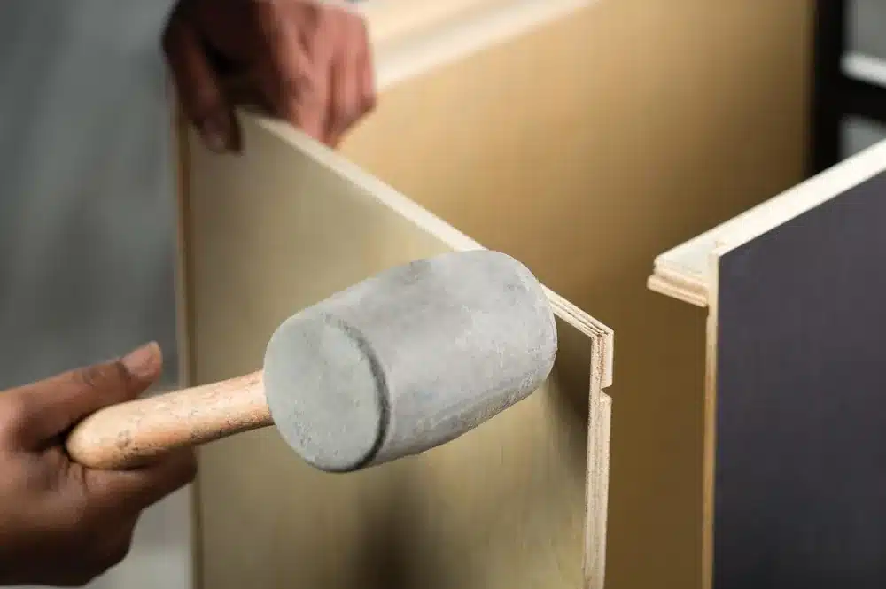 Rubber mallet striking the back panel of a Fabuwood cabinet box